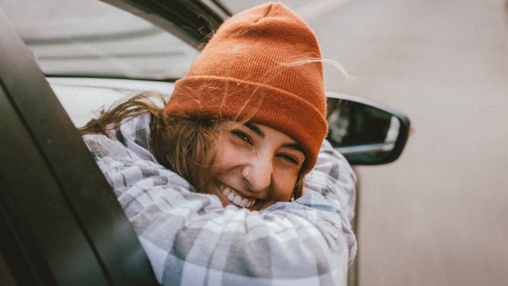 woman with beanie looks out car window smiling