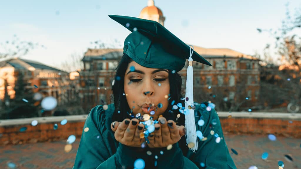 college graduate blowing confetti