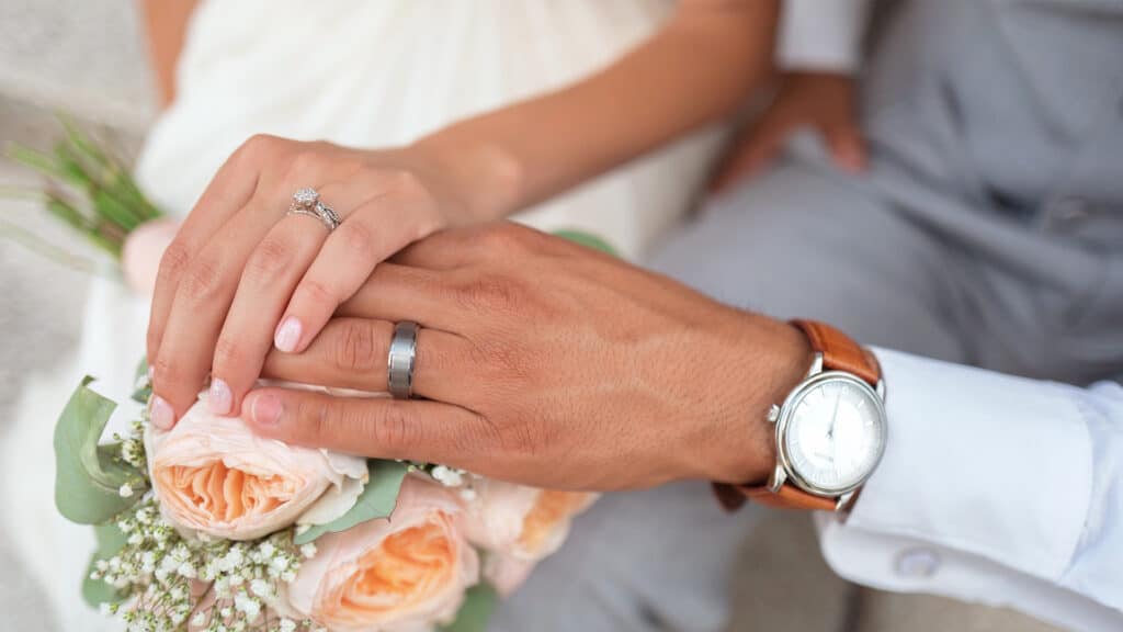 wedding rings on hands over flowers